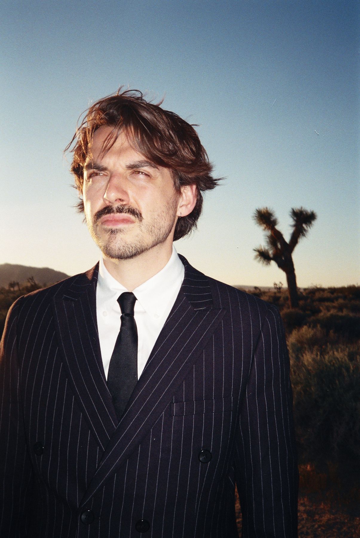 Portrait of Yes in a pinstripe suit in the desert at golden hour